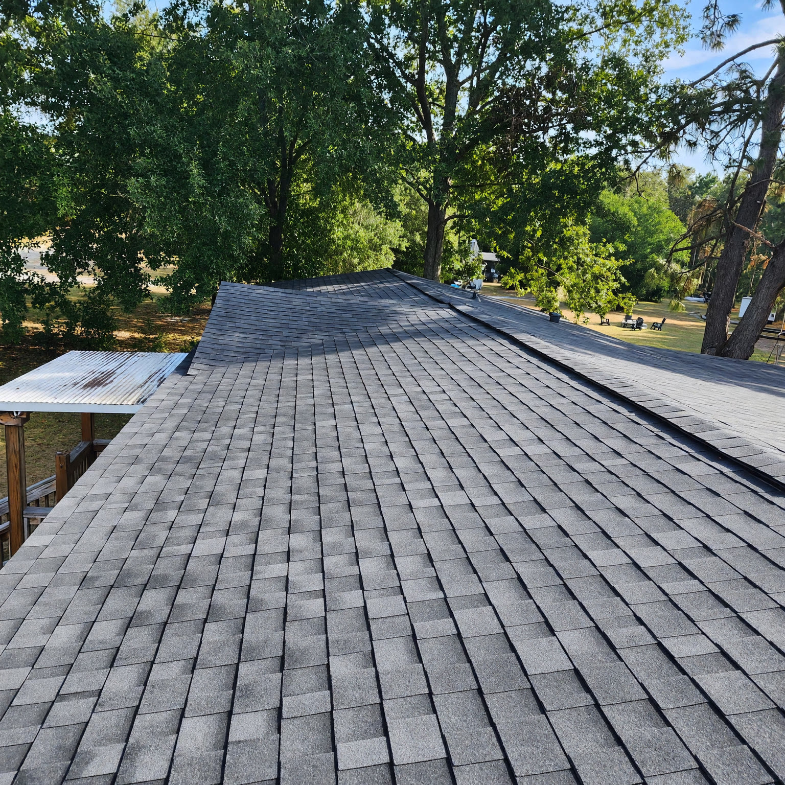 Finished architectural shingle roof photographed from the ridge, treeline and yard beyond