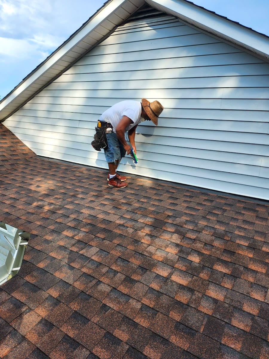 An Ole South roofer fastening trim on a gable above a freshly laid architectural shingle roof