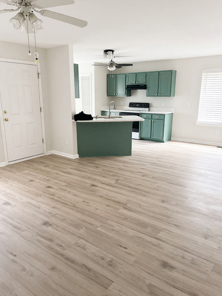 Kitchen with teal-green cabinets and island, new LVP floor running into the living room