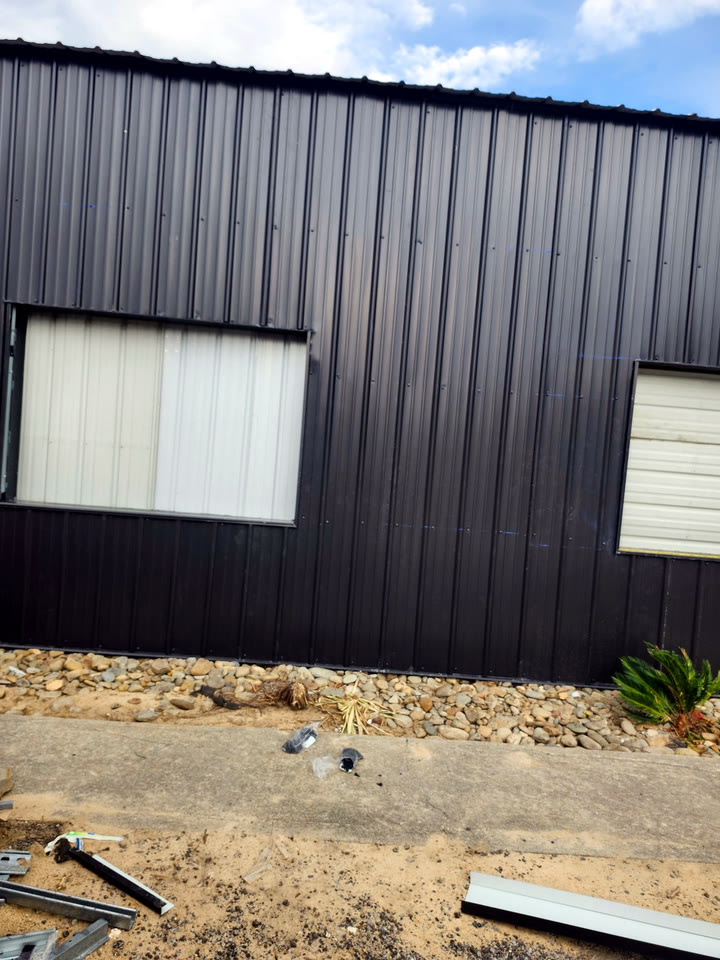 Dark vertical corrugated metal wall with new windows, river rock along the base