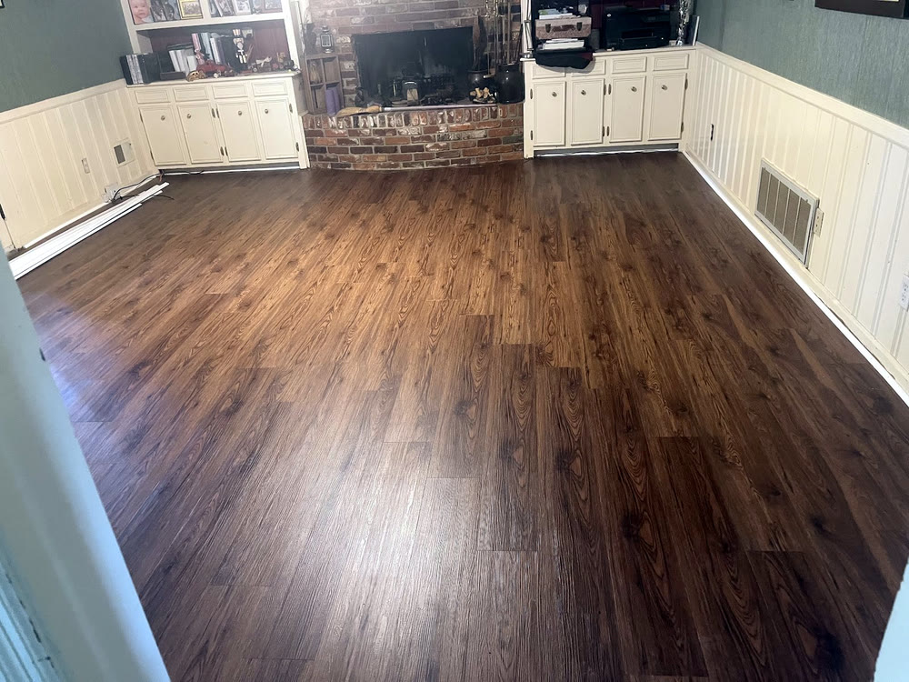 New dark LVP floor across a living room — white wainscot, teal walls, brick fireplace